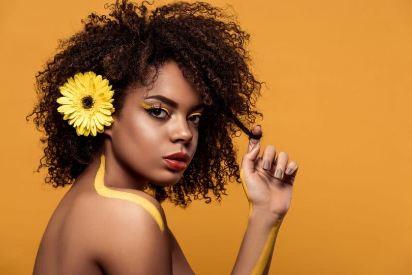 Mulher negra com uma flor amarela no cabelo.