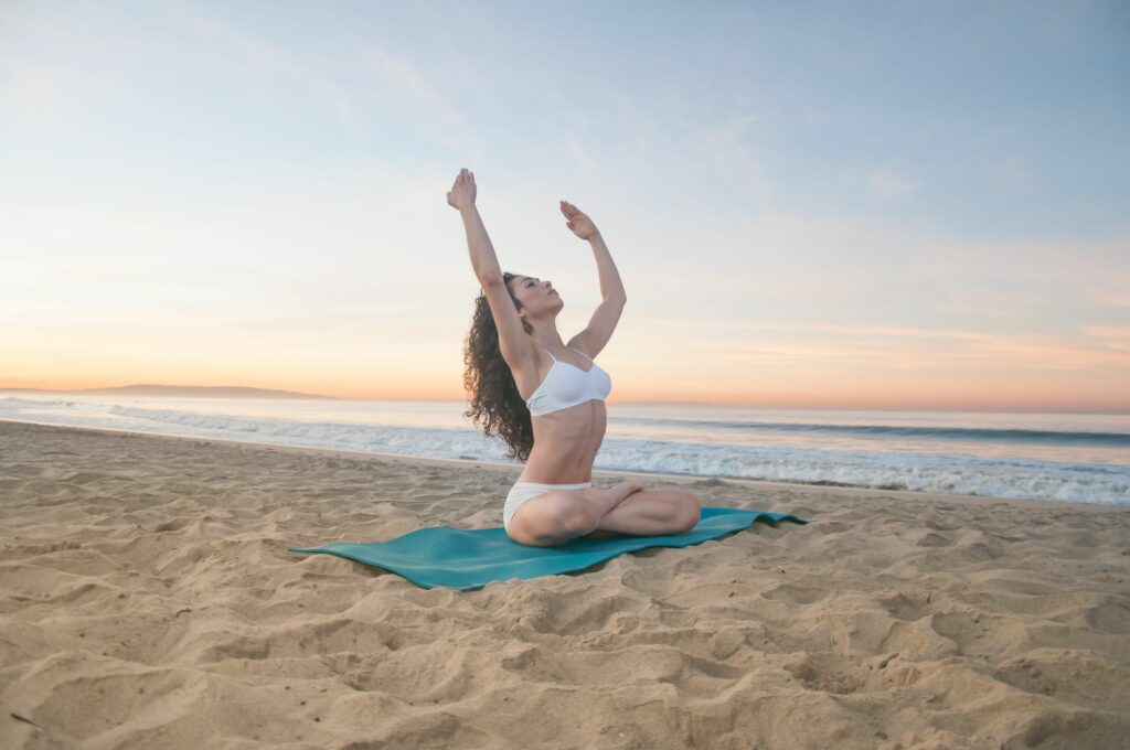 Mulher meditando em uma praia com as mãos para cima.