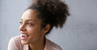 Mulher negra com cabelo preso sorri e olha para o lado