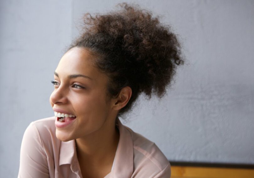 Mulher negra com cabelo preso sorri e olha para o lado