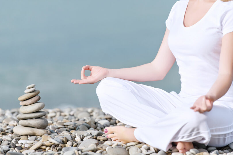 mão de uma mulher meditando em uma pose de ioga na praia