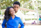 Casal hétero negro posando para foto abraçados com paisagem de parque ao fundo.