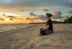 Mulher em posição meditativa sentada na areia.