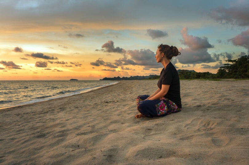 Mulher em posição meditativa sentada na areia.