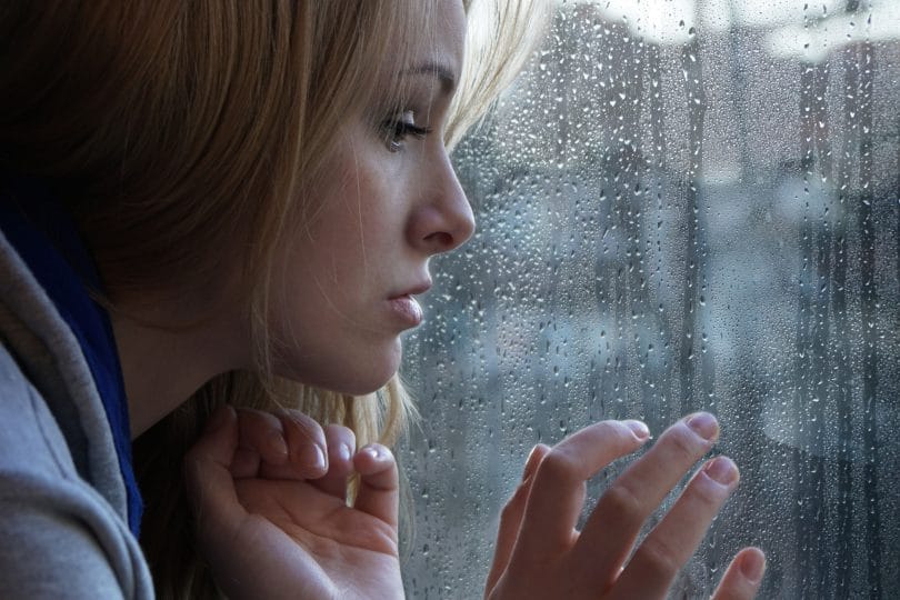 Mulher triste olhando através da janela em um dia chuvoso.