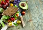 Sanduíche vegano com ingredientes frescos: abacate, alface, tomate, cenoura, repolho roxo e uma faca.