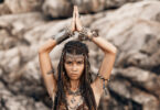 Foto de mulher morena vestida de índia com as mãos juntas em cima da cabeça.