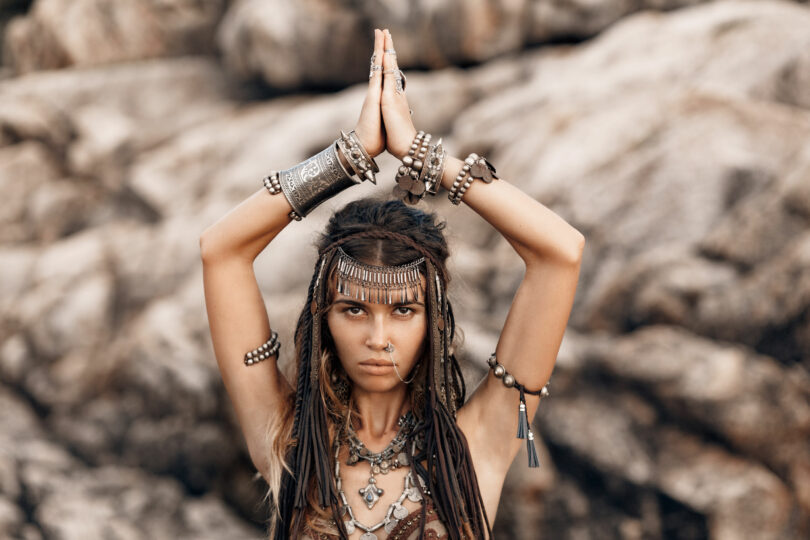 Foto de mulher morena vestida de índia com as mãos juntas em cima da cabeça.