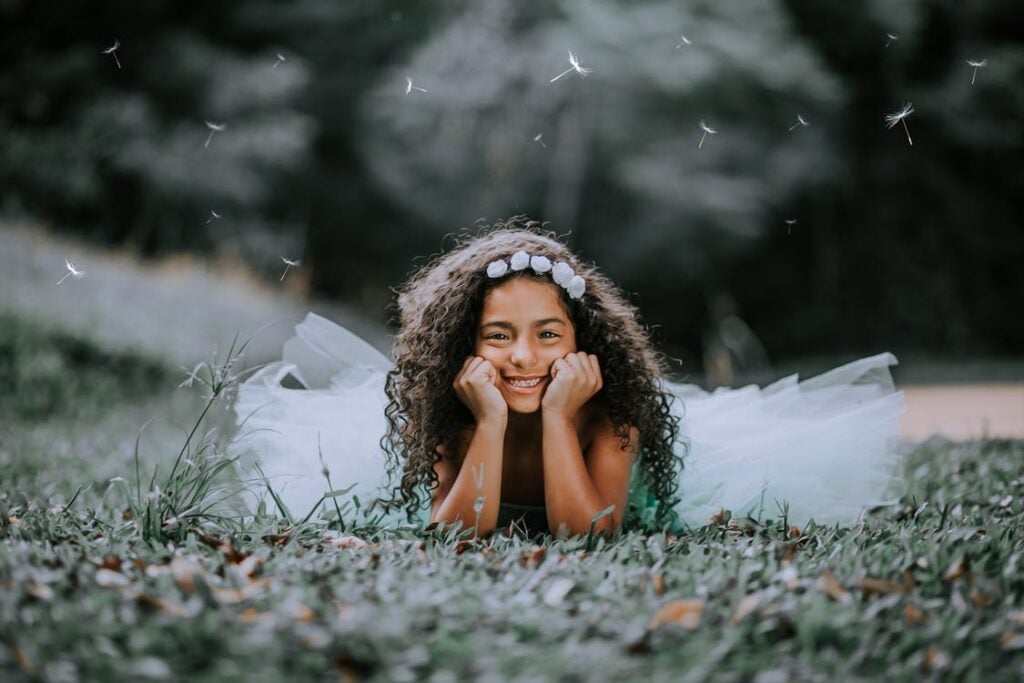 Menina de cabelos crespos deitada na grama sorrindo.