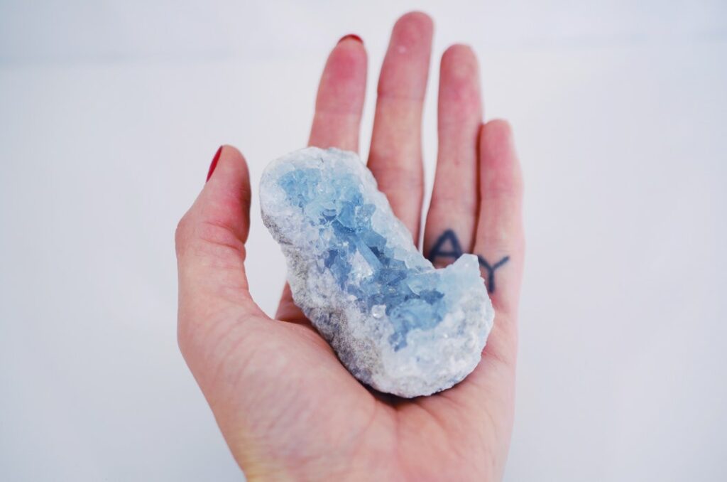 Mão segurando um cristal azul claro com detalhes em branco.