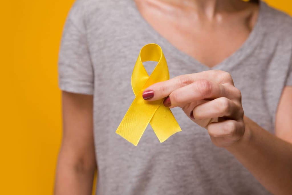 Mulher em fundo amarelo, segurando uma fita amarela em sinal de conscientizar sobre a endometriose.