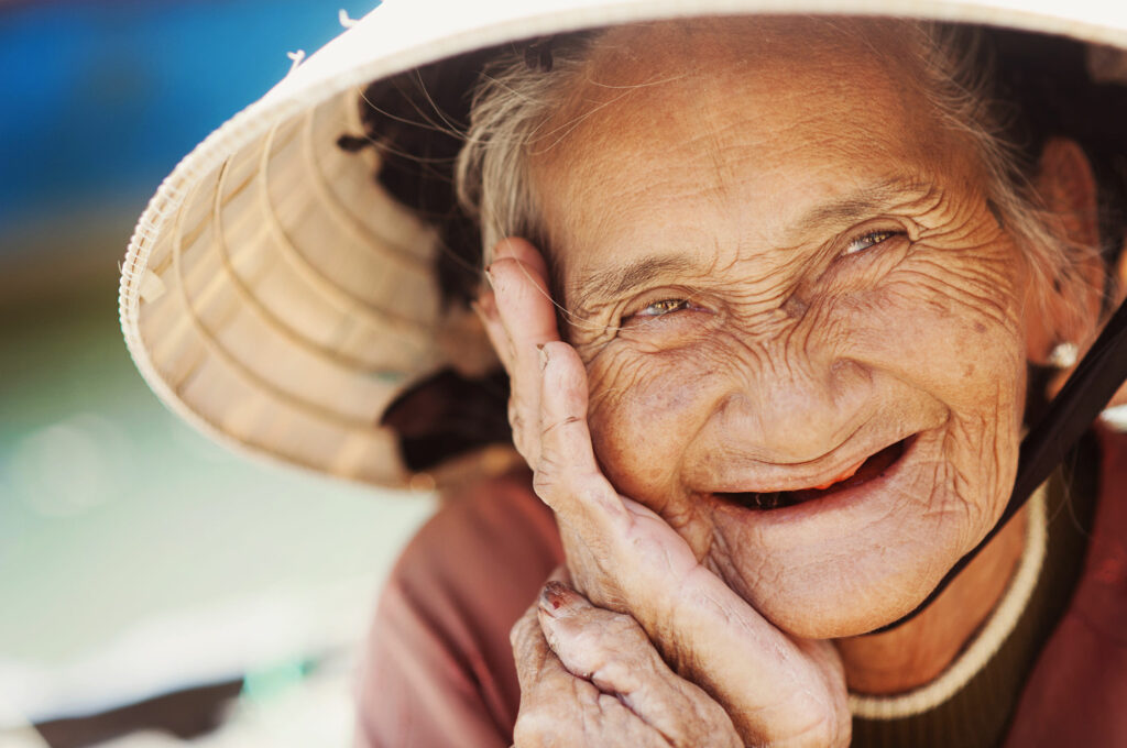 Senhora de idade sorridente, com o rosto cheio de rugas e marcas de expressão.