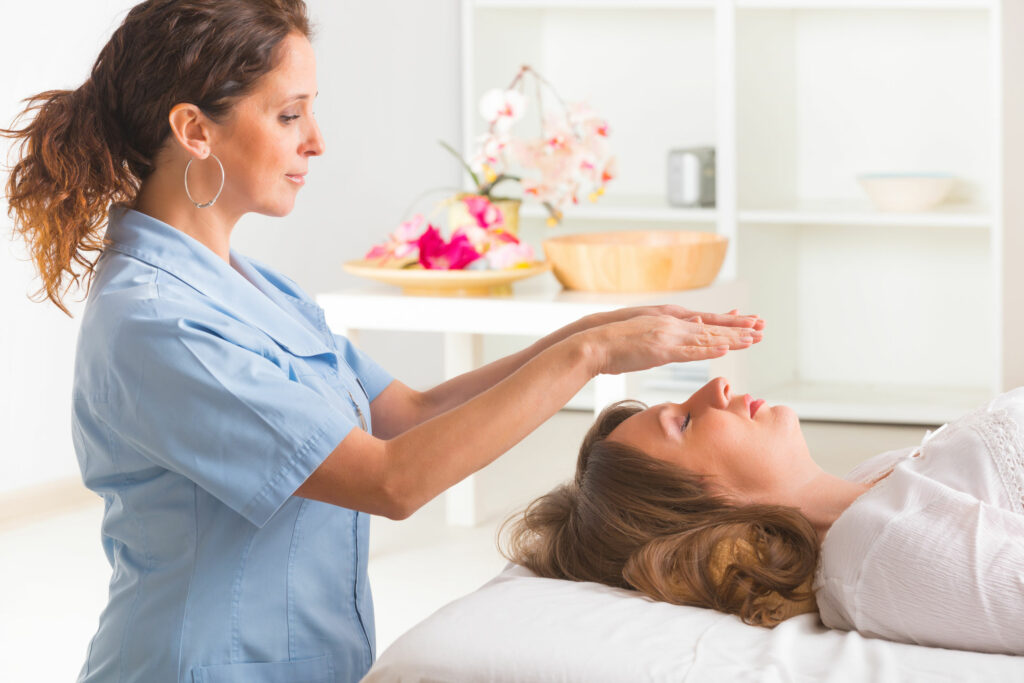 Profissional usando a técnica de Reiki para tratar jovem mulher. Angulo lateral para a curandeira.