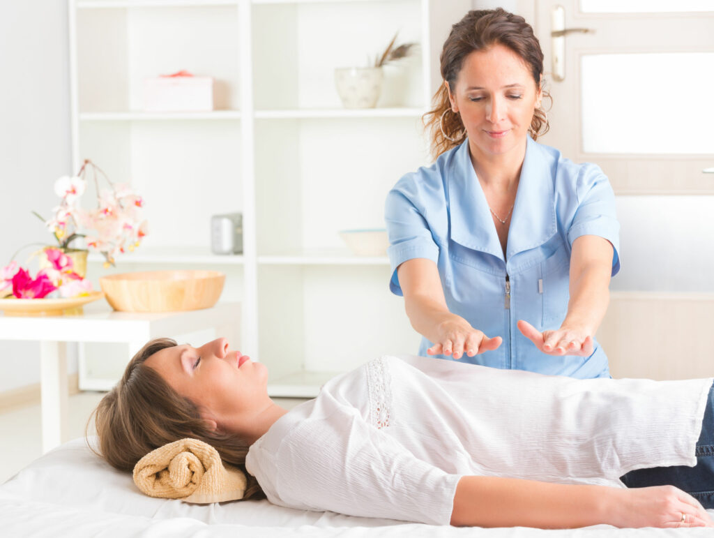 Profissional usando a técnica de Reiki para tratar jovem mulher. Angulo frontal para a curandeira.