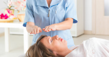 Profissional usando a técnica de Reiki para tratar jovem mulher.