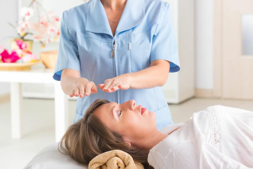 Profissional usando a técnica de Reiki para tratar jovem mulher.