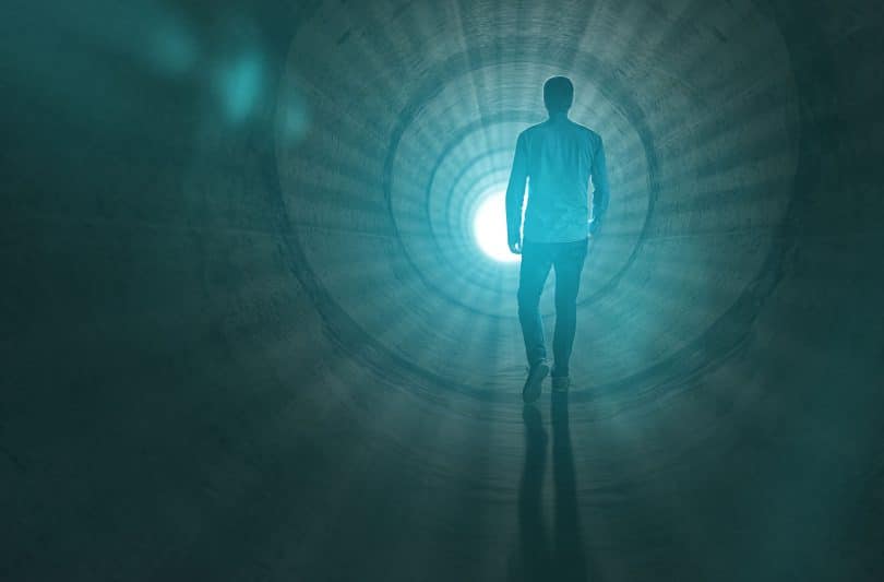 Homem caminhando para a luz no fim do túnel