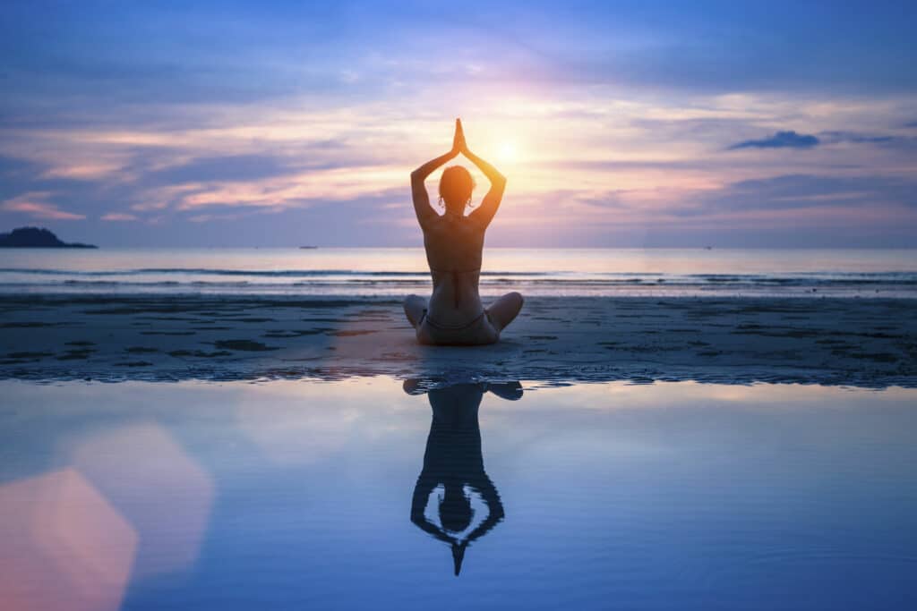 Silhueta de pessoa meditando na praia ao pôr do sol.