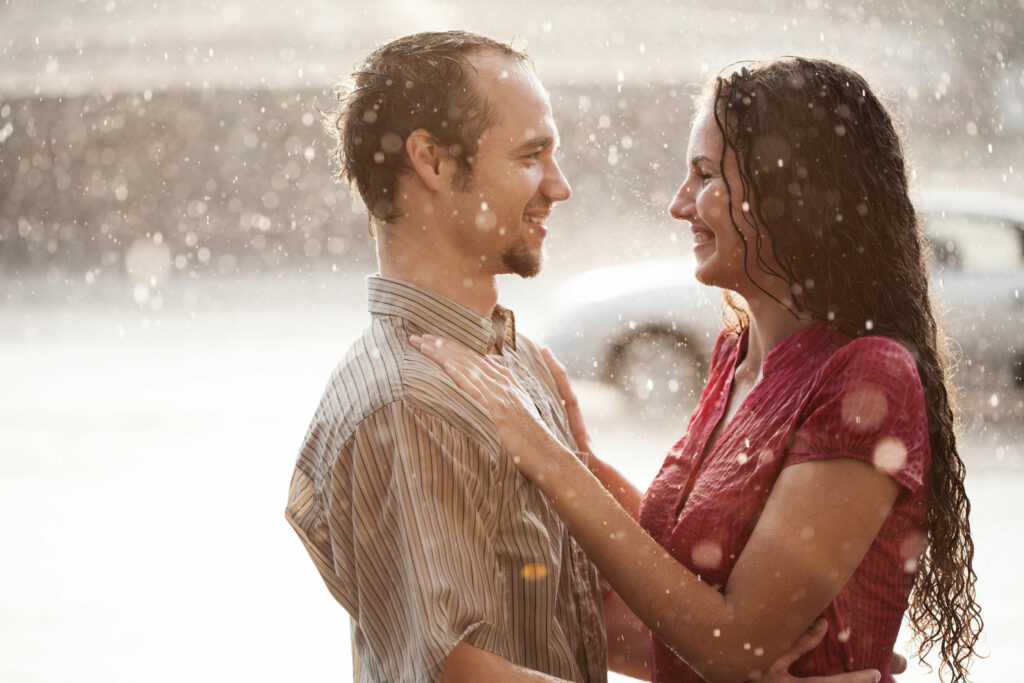 Casal tomando chuva juntos de frente um para o outro.