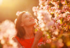 Mulher jovem e sorridente observando as flores em um jardim num dia ensolarado.