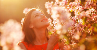 Mulher jovem e sorridente observando as flores em um jardim num dia ensolarado.