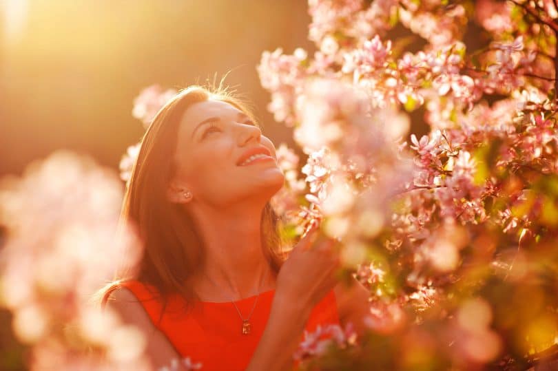 Mulher jovem e sorridente observando as flores em um jardim num dia ensolarado.