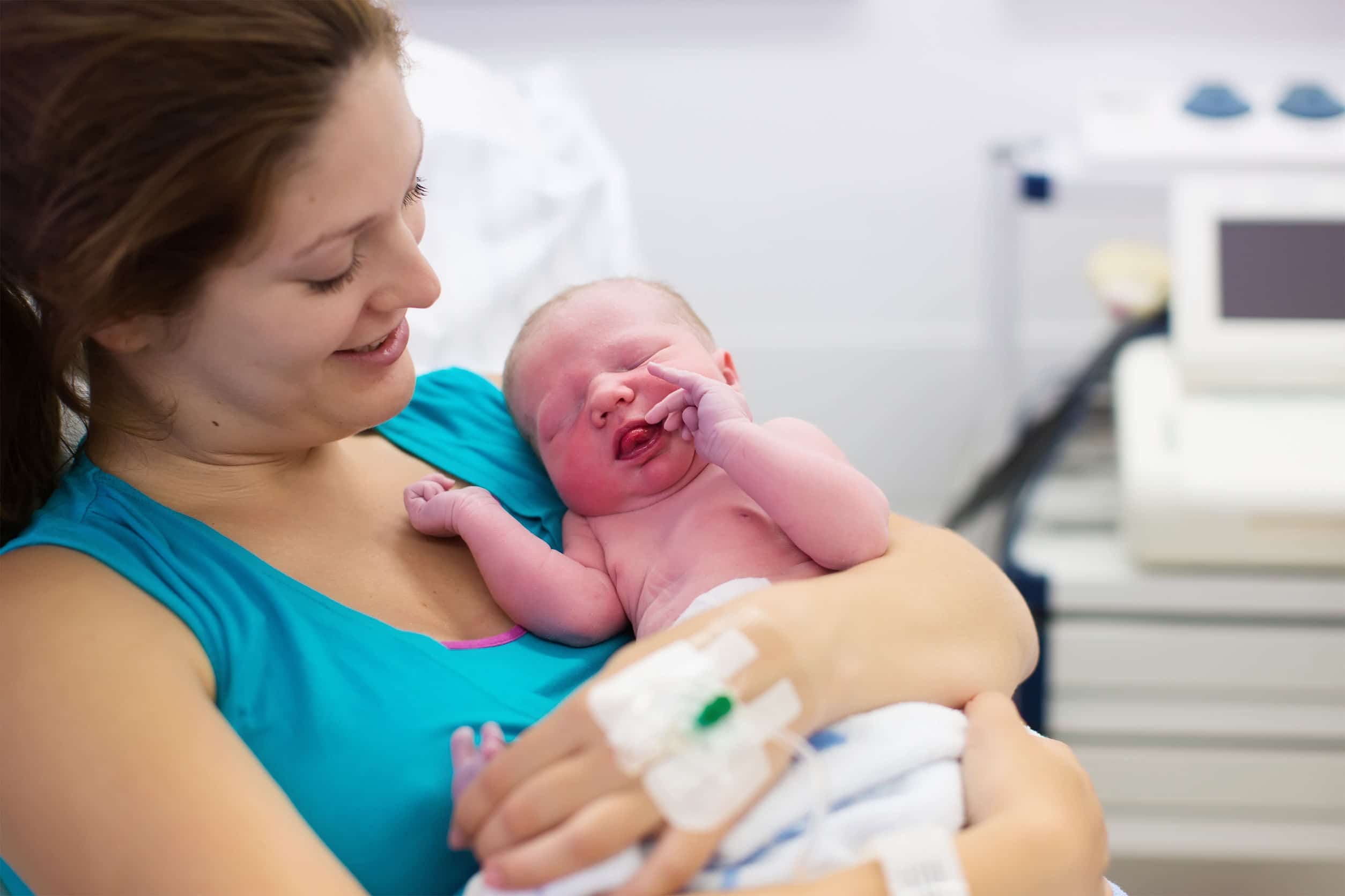 Mulher branca jovem segurando um bebê recém nascido logo após de dar a luz.
