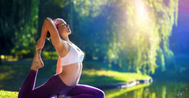 Mulher praticando yoga, vestindo roupas de ginástica, em um parque, próximo à um lago.