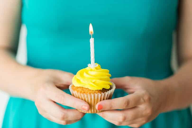 Mulher segura cupcake de cobertura amarela com uma vela acesa.