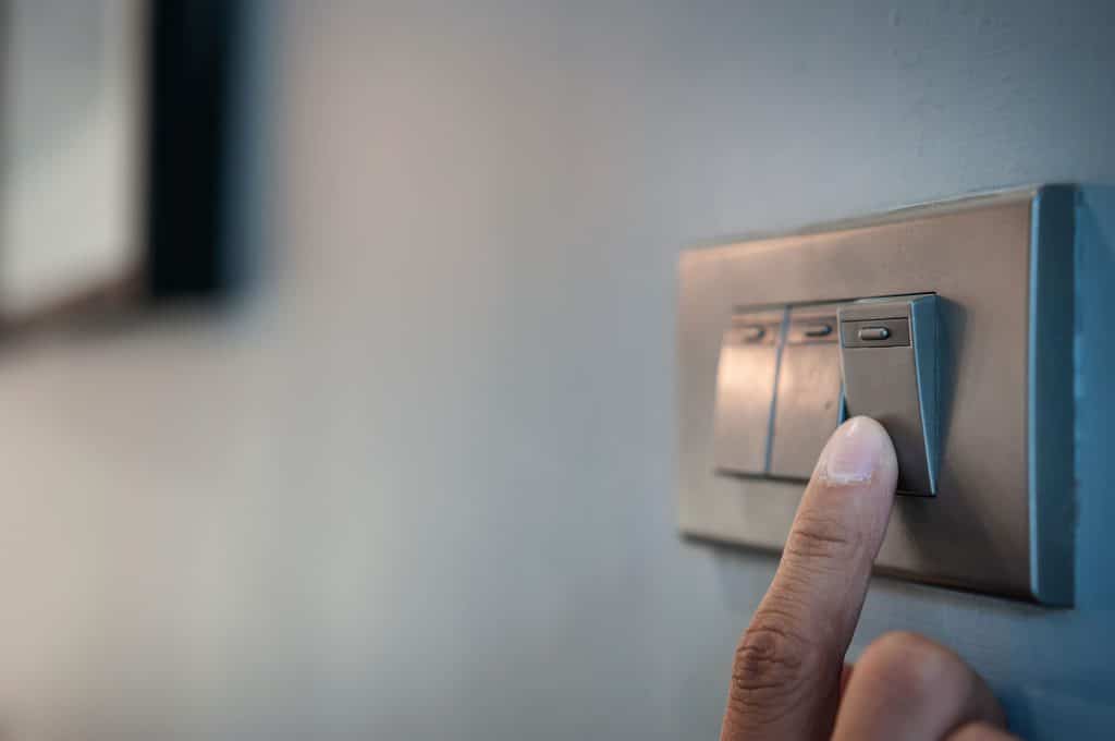 Foto de dedo humano apagando interruptor de luz em uma parede branca.