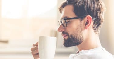 Homem sorrindo e segurando uma xícara de café.