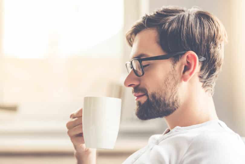 Homem sorrindo e segurando uma xícara de café.