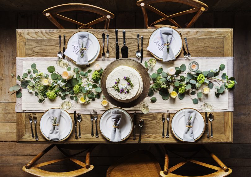 Mesa pratos postos e bolo no meio. Decoração de folhas e flores.