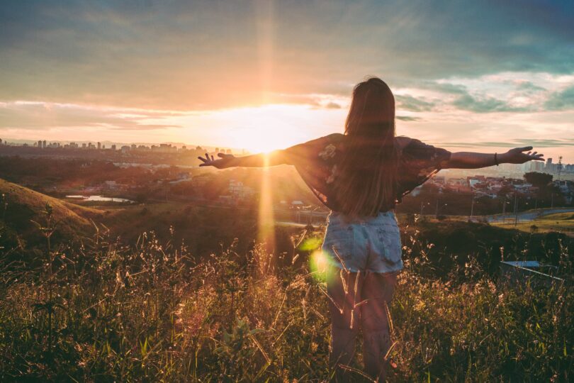 Menina em montanha com os braços abertos. Fundo de pôr-do-sol.