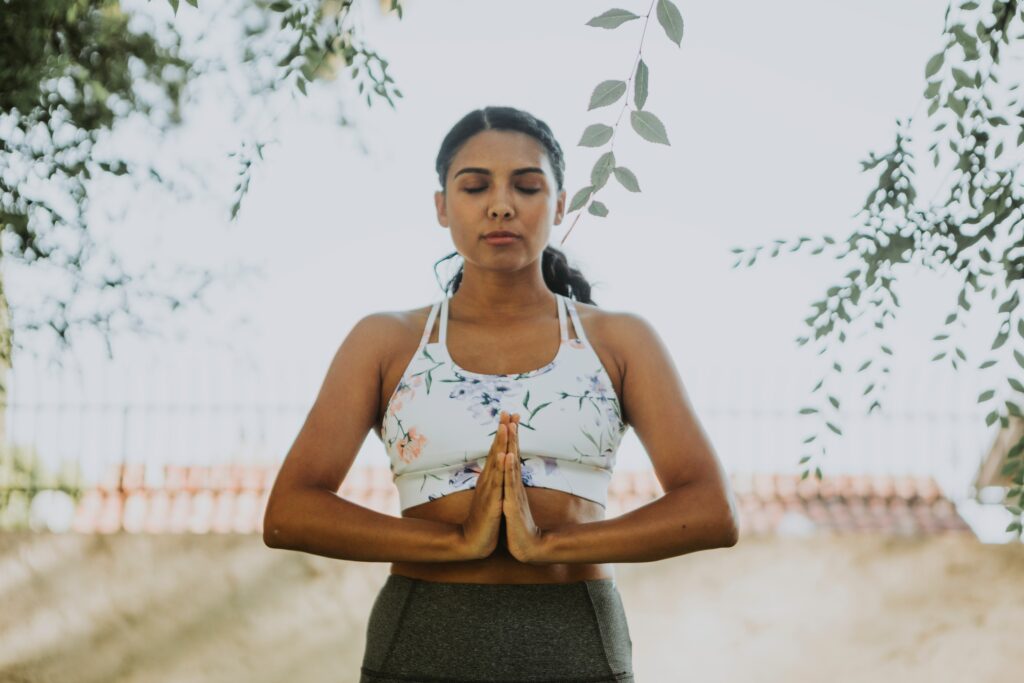 Mulher meditando. Fundo de céu e galhos de árvores.