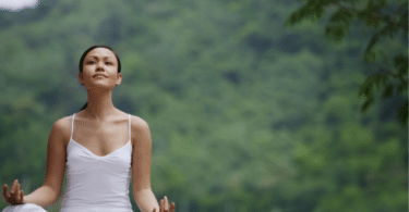 Mulher meditando. No fundo, há várias árvores