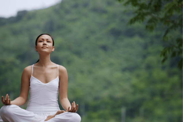 Mulher meditando. No fundo, há várias árvores