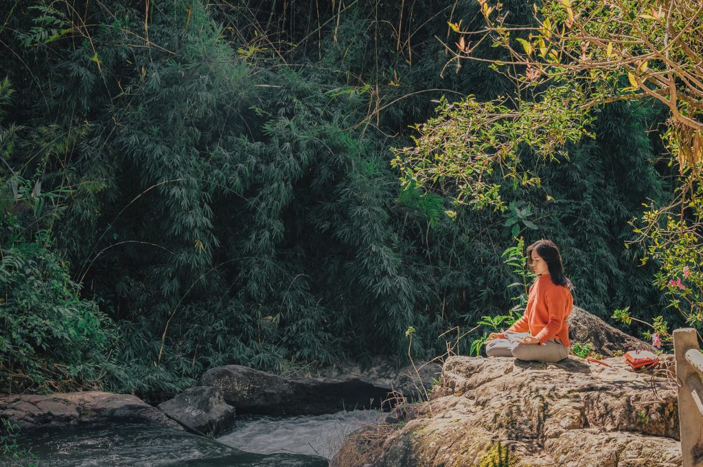 Mulher asiática meditando em cima de uma pedra.