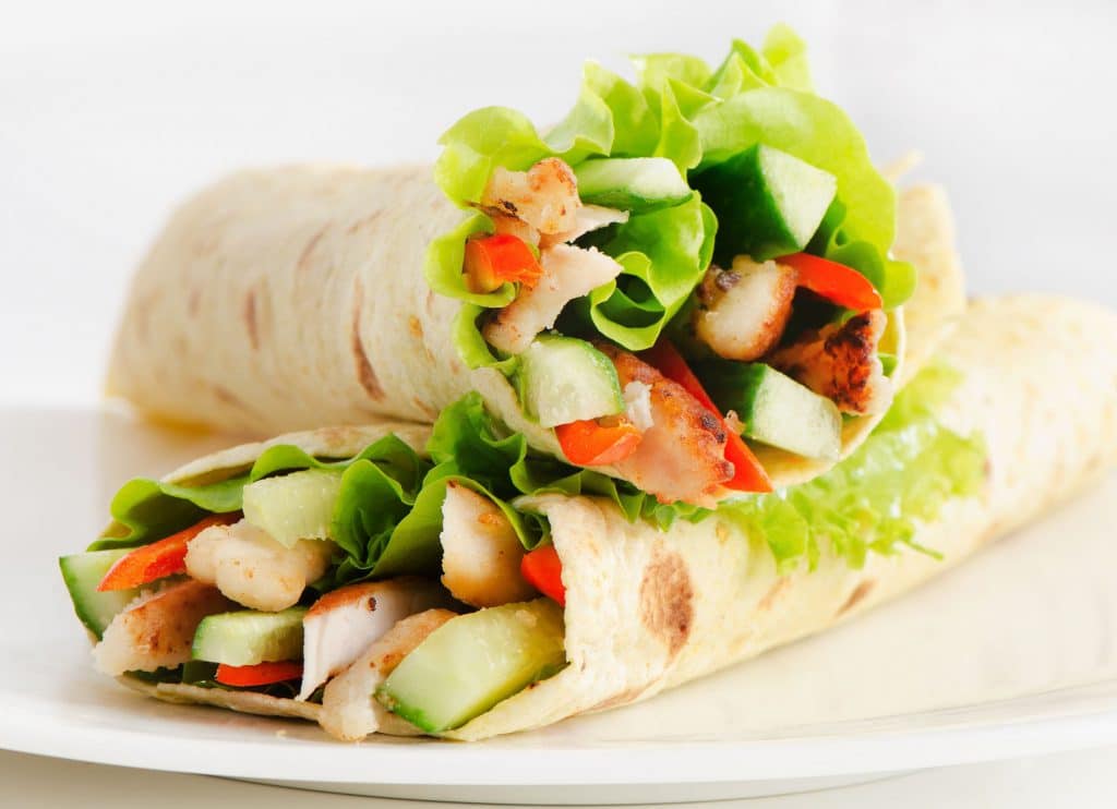 Dois wraps de grão de bico, recheado com vegetais e saladas, em um prato branco.