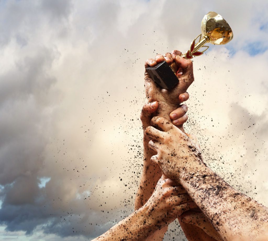 Mão de diversas pessoas lutando para segurar um troféu com uma pequena taça de ouro