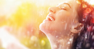 Mulher feliz, sorridente, tomando chuva no rosto.