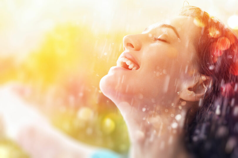 Mulher feliz, sorridente, tomando chuva no rosto.