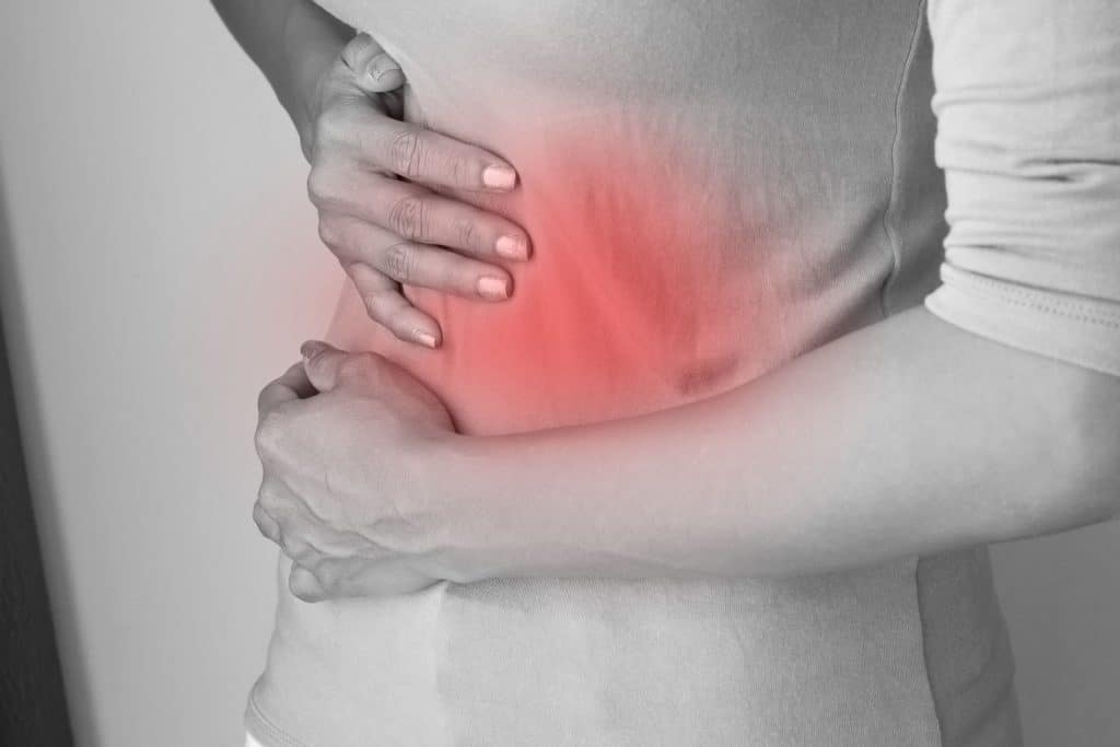 Foto preta e branca de mulher com dor no abdome , apoiando suas mãos em um ponto vermelho em cima do seu ventre.
