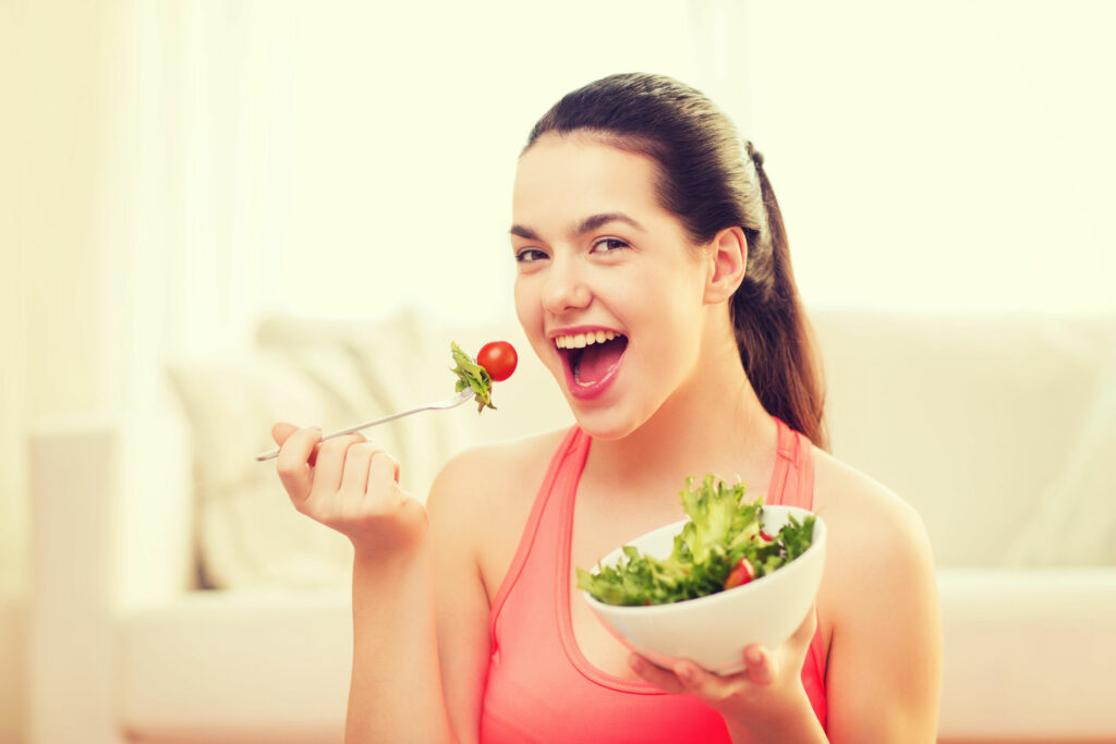 Mulher comendo salada e sorrindo para câmera.