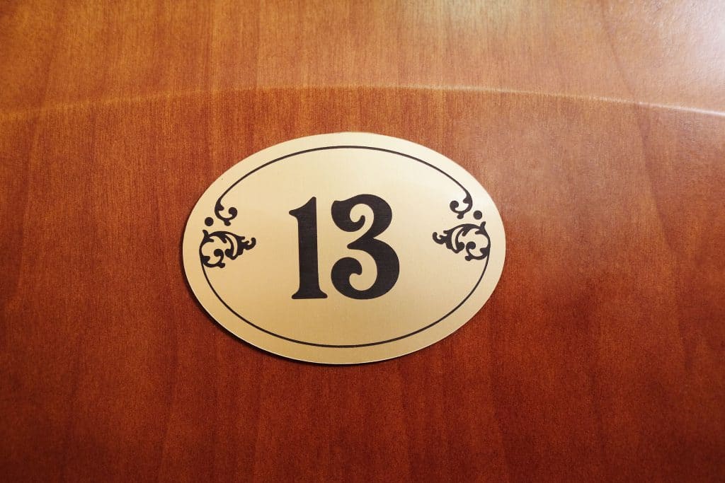 Porta de madeira escura, com placa dourada com o número 13 escrito em preto.