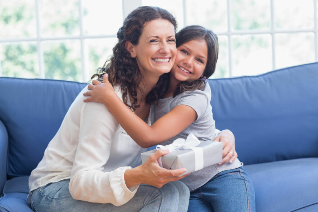 Mãe e filha criança sorridentes sentadas ambas em um grande sofá azul.