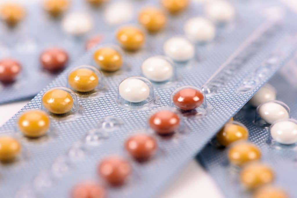 Diversas cartelas de pílulas anticoncepcional empilhadas uma em cima da outra, em uma mesa branca.