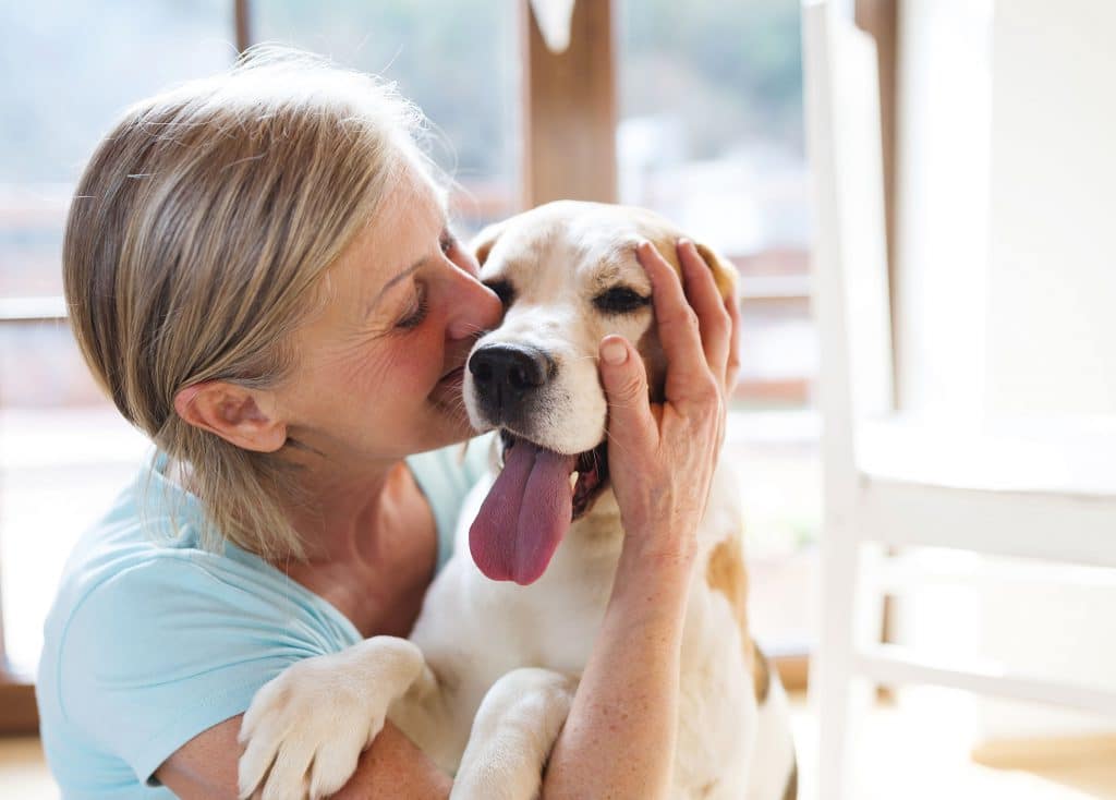 Mulher branca, feliz, abraçando um cachorro golden, que está feliz com a língua para fora.