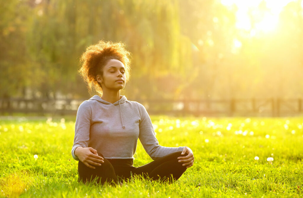 Mulher negra sentada na grama com as pernas cruzadas meditando