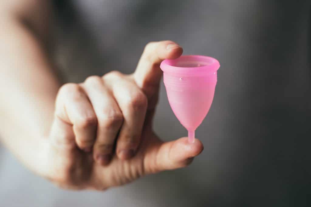 Close de mão de mulher segurando um coletor menstrual rosa.